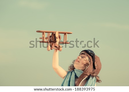 Happy child playing with toy wooden airplane. Smiling kid against summer sky background. Retro toned. Travel and adventure concept