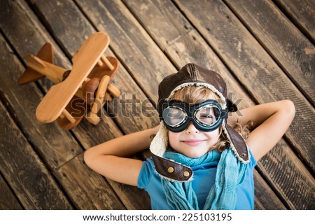 Child pilot with vintage plane toy on grunge wooden background