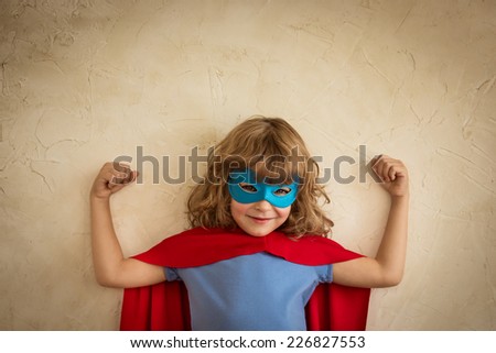 Superhero child against grunge wall background. Kid playing at home. Girl power concept