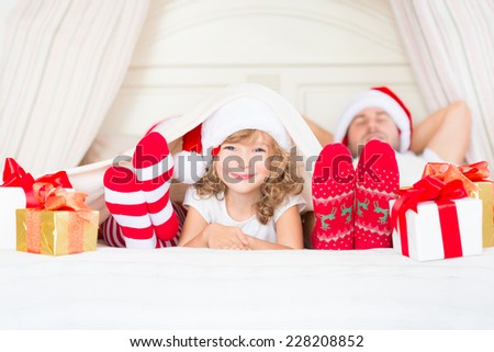 Happy family at home. Mother, father and child lying in the bed with Christmas gift. Winter holiday concept
