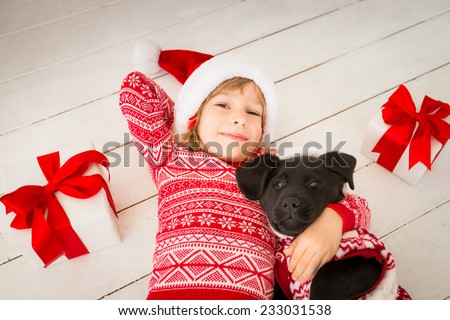 Happy child and dog with Christmas gift. Kid dressed in Santa Claus hat. Baby having fun at home. Xmas holiday concept