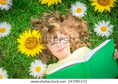 Happy child lying on green grass. Funny kid reading the book in spring park