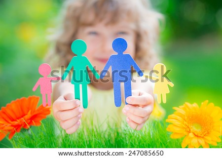 Child holding multi ethnic paper family in hands against spring green background