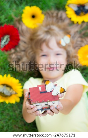 Beautiful child with butterfly in spring park. Happy kid holding house in hand. Real estate concept
