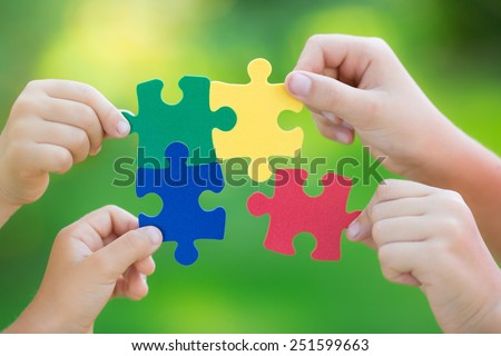 Multicolor puzzles in hands against green spring blurred background. Teamwork and solution concept
