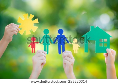 Paper house and family in hands against spring green background. Real estate business concept