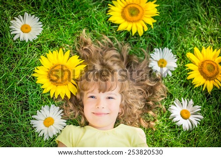 Happy child lying on grass. Funny kid playing in park. Beautiful spring flowers