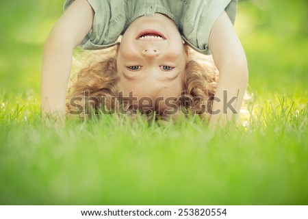 Happy child standing upside down on green grass. Laughing kid having fun in spring park. Healthy lifestyle concept