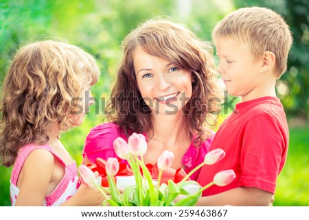 Happy family with bouquet of flowers and gifts outdoors. Young beautiful mother with son and daughter lying on green grass. Spring holiday concept. Women\'s day concept