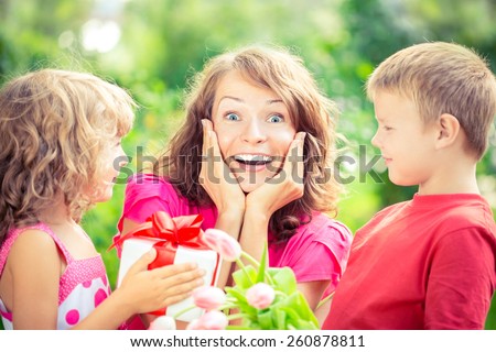 Happy family with bouquet of flowers and gifts outdoors. Young beautiful mother with son and daughter lying on green grass. Spring holiday concept. Mother\'s day. Surprise and joy