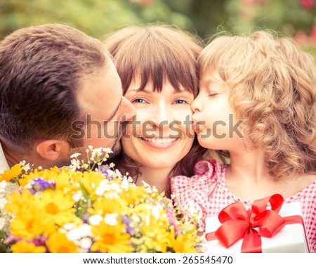 Happy family with gift box and beautiful flowers against green background. Spring holiday concept. Mothers day