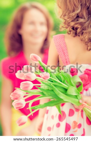 Woman and child with bouquet of flowers against green blurred background. Spring family holiday concept. Women\'s day