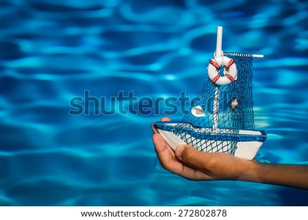 Summer vacation concept. Toy sailing boat in hands on the water background