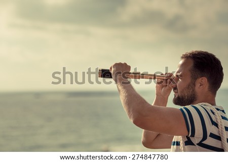Sailor man looking through the binoculars against blue sky background