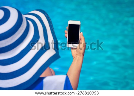 Woman holding smart phone in hand against blue water background. Summer vacation concept