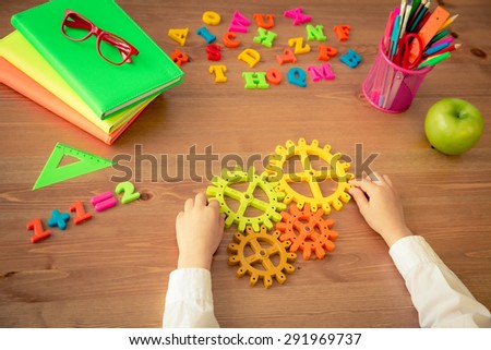 Child holding gear in hands. School items on wooden desk in class. Education concept. Top view