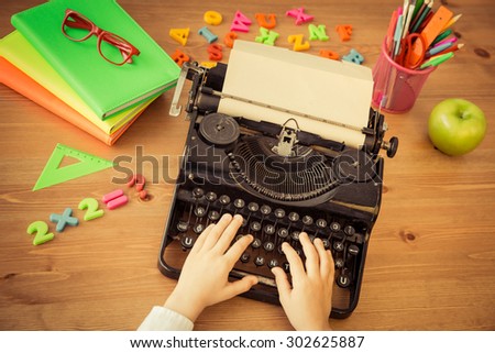 Child operate on manual vintage typewriter. School items on wooden desk in class. Education concept. Top view