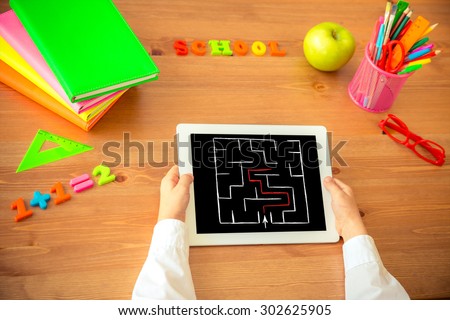 Child holding tablet PC in hands. School items on wooden desk in class. Education concept. Top view