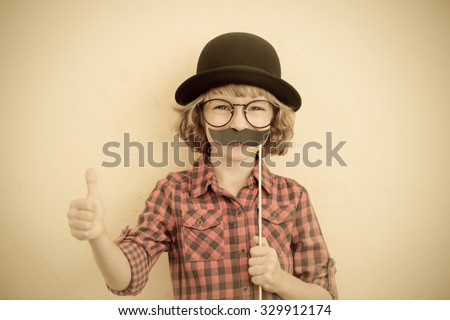 Funny kid with fake mustache. Happy child playing in home