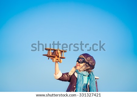 Kid pilot with toy wooden airplane against blue winter sky background. Happy child playing outdoors