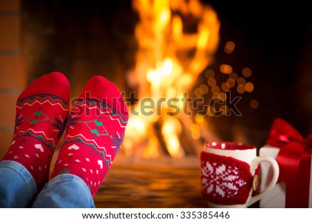 Woman at home. Feet in Christmas socks near fireplace. Relaxing and comfort. Winter holiday concept
