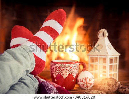 Woman at home. Feet in Christmas socks near fireplace. Relaxing and comfort. Winter holiday concept