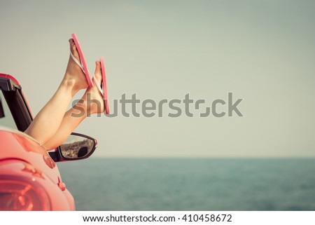 Young woman relaxing on the beach. Girl having fun in red cabriolet against toned sky background. Summer vacation and travel concept