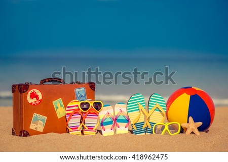 Vintage suitcase and flip-flops on sandy beach against blue sea and sky background. Summer vacation concept