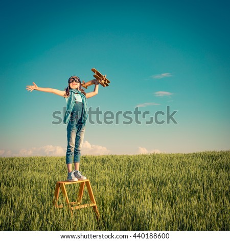 Happy child playing outdoors. Kid having fun in summer field. Child with toy airplane. Kid pretend to be pilot. Travel, vacation and freedom concept. Childhood, imagination, dream
