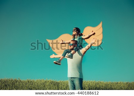 Happy family outdoors. Child playing with father. Dad and son having fun in summer field. Man carrying kid. Child with cardboard wings. Kid pretend to be pilot. Imagination and freedom concept