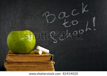Chalk and green apple on old textbook against blackboard with text BACK TO SCHOOL in class. School concept