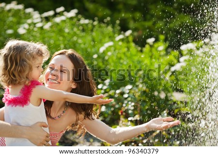 Woman with child playing against splashes of water in the summer