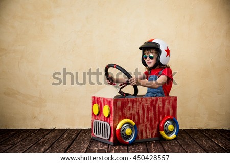 Child driving a car made of cardboard box. Kid having fun indoors. Child playing at home. Dream, imagination, childhood. Travel and summer vacation concept