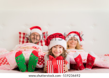 Family in Christmas Santa hats lying on bed. Mother; father and child having fun in bedroom. People relaxing at home. Kid holding gift box. Winter holiday Xmas and New Year concept