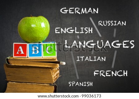 Green apple and ABC on old books against blackboard with with the drawn scheme of studying of languages. School concept