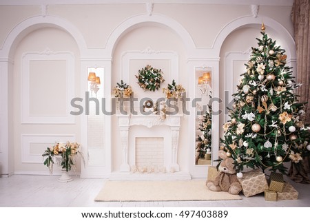 Majestic white hall with classical fireplace, arches and mirrors. At the wall hanging Christmas wreath. New Year tree stands in the corner of room.