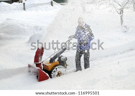 Man is making a path by removing snow with snow blower after winter storm.