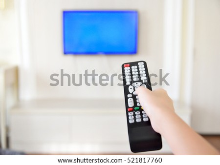 Hand holding tv remote control and surfing programs on television. Teenage girl watching TV in the living room or bedroom. copy space.