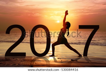 Happy new year card 2017. Silhouette of A girl doing Yoga warrior I pose on tropical beach with sunset sky background, practicing yoga on the beach, standing as a part of the Number 2017 sign.