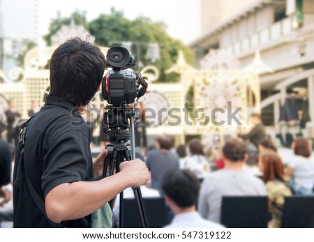 Back of young cameraman using a professional camcorder outdoor  filming music show or mini concert with blur background, Bangkok, Thailand