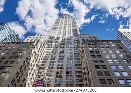 Towering classic New York City architecture against a blue cloud filled sky.