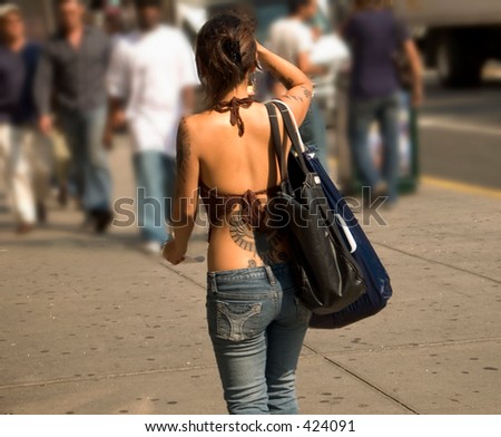 This is a shot of a young lady with several tattoos walking in the city.