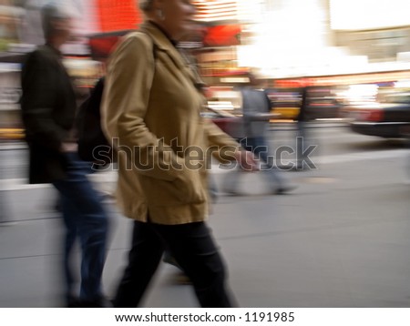 A motion blur of a woman and others walking down a busy Manhattan street.