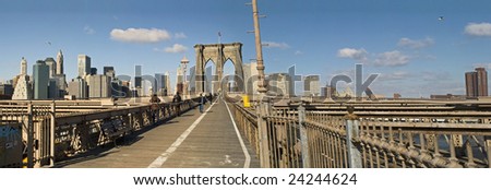 A panoramic view of the pedestrian walkway across the Brooklyn Bridge with the skyline of Manhattan in the background.