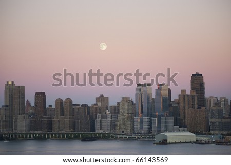 A full moon in daytime rises up over Manhattan and the West Side Highway as seen from across the Hudson River in New Jersey.