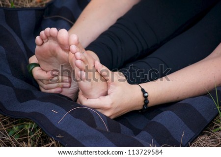 Close up of hands and feet of woman doing yoga forward fold outdoors on striped mat.