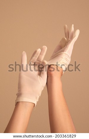 A woman\'s hands and forearms are shown as she models a vintage pair of formal white gloves. She is using one gloved hand to pull the glove onto the other hand.