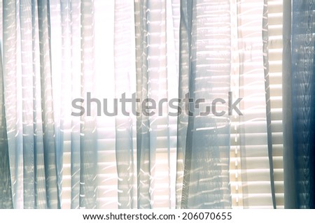 Bright daylight shines through a window draped with blue sheer curtains in this semi abstract high key image.