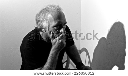 An older white man is looking away with a concerned look on his face and covering his mouth.