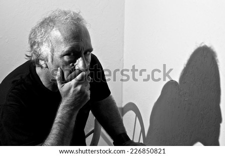 An older white man is looking directly at viewer with a serious look in his eyes and covering his mouth with his hand.